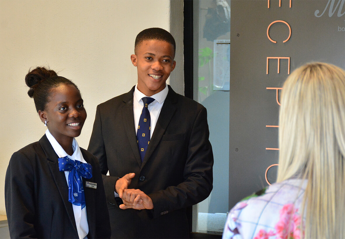 Two young professionals in formal attire engaging in conversation at a reception area.