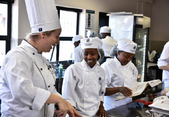 Culinary students in white chef uniforms engaged in a cooking class with an instructor.